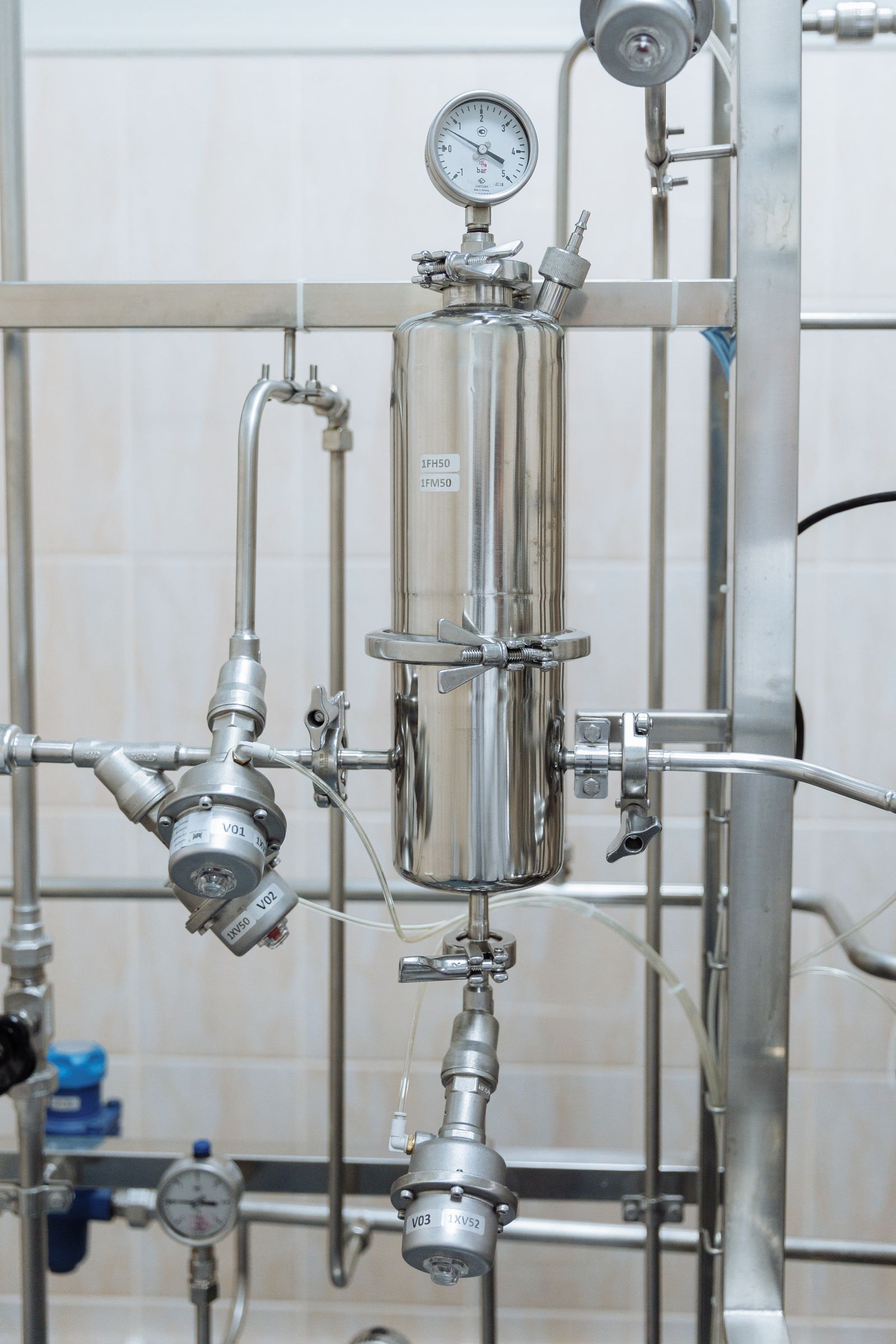 Stainless steel fluid line with gauges, valves, and a small process vessel.